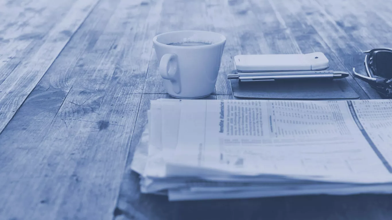 Zeitung liegt auf Holztisch mit Kaffeetasse und Smartphone